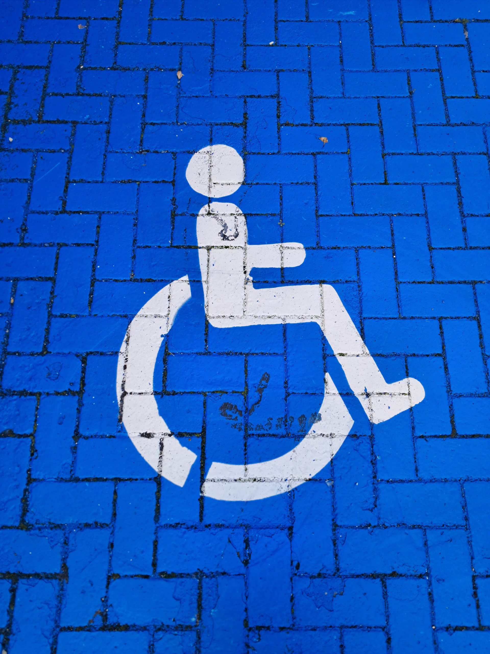 White wheelchair symbol on a blue brick parking spot denoting accessibility.