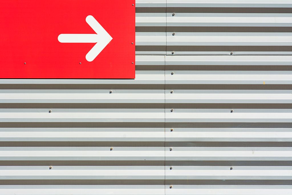Minimalist image featuring a red arrow sign on a corrugated metal wall.