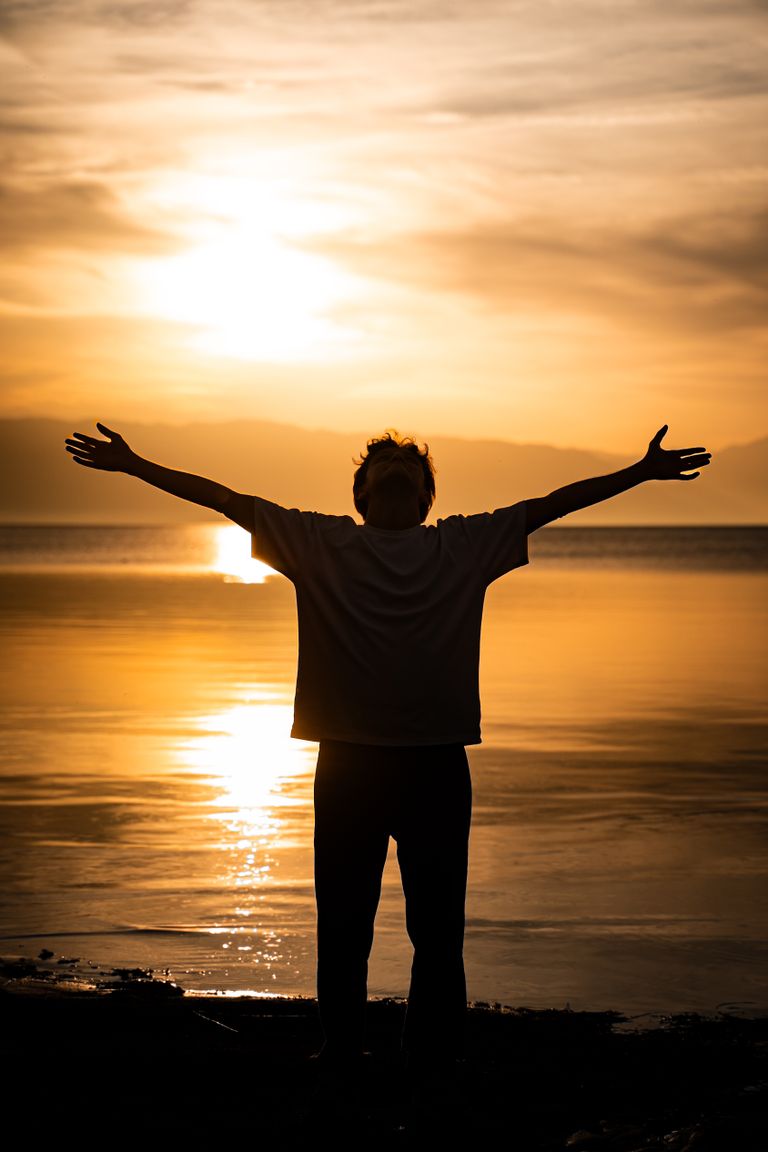 Silhouette of a person with arms outstretched during sunset on a serene lakeside.