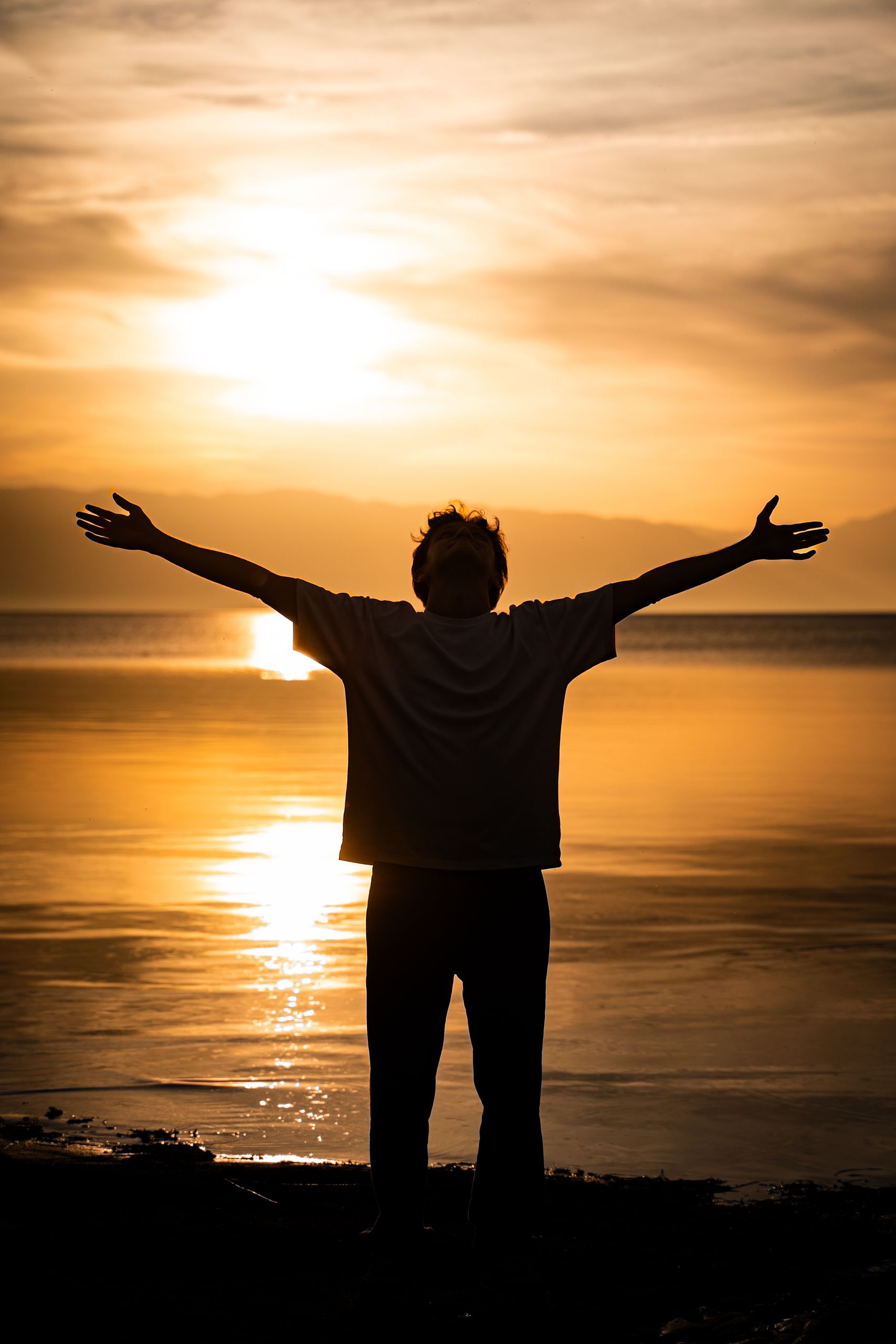 Silhouette of a person with arms outstretched during sunset on a serene lakeside.